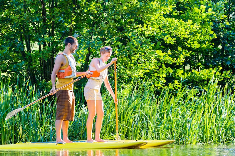 Friends paddling with surfboard sup on forest river